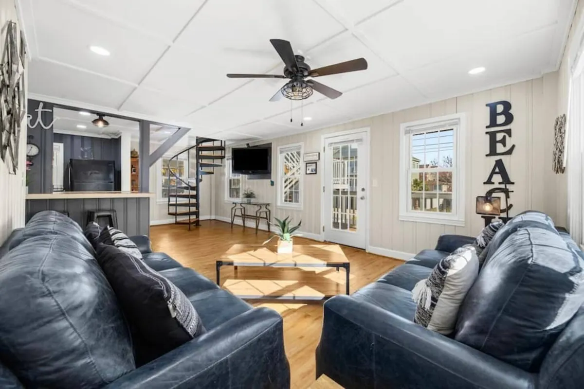 This image features comfortable couches arranged for socializing, a spiral staircase as an architectural centerpiece, a coffee table with decorative accents, and a wall-mounted TV. The space is well-lit and designed for both relaxation and entertainment.