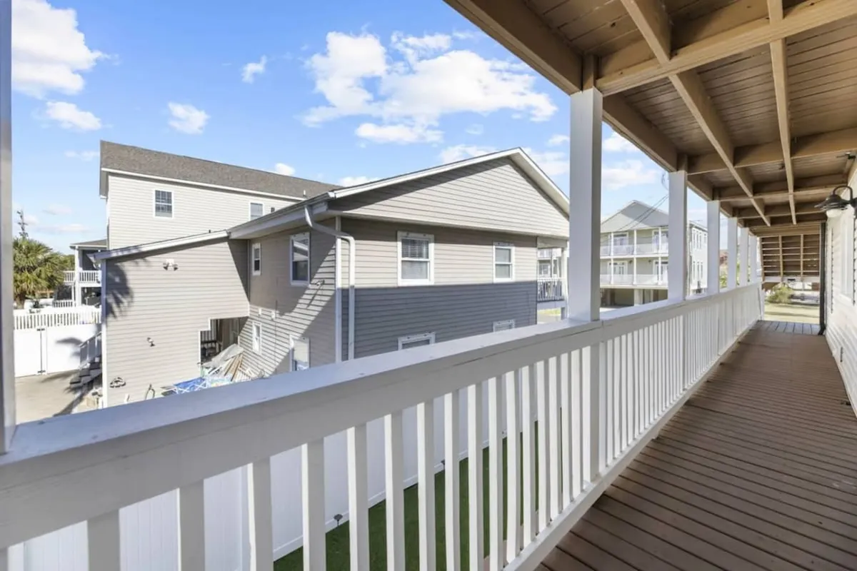 An exterior shot from the balcony, featuring a wooden deck and a view of neighboring buildings. The scene captures the tranquil mood of relaxing outdoors, with sunlight and fresh air inviting guests to unwind and connect with the surroundings.