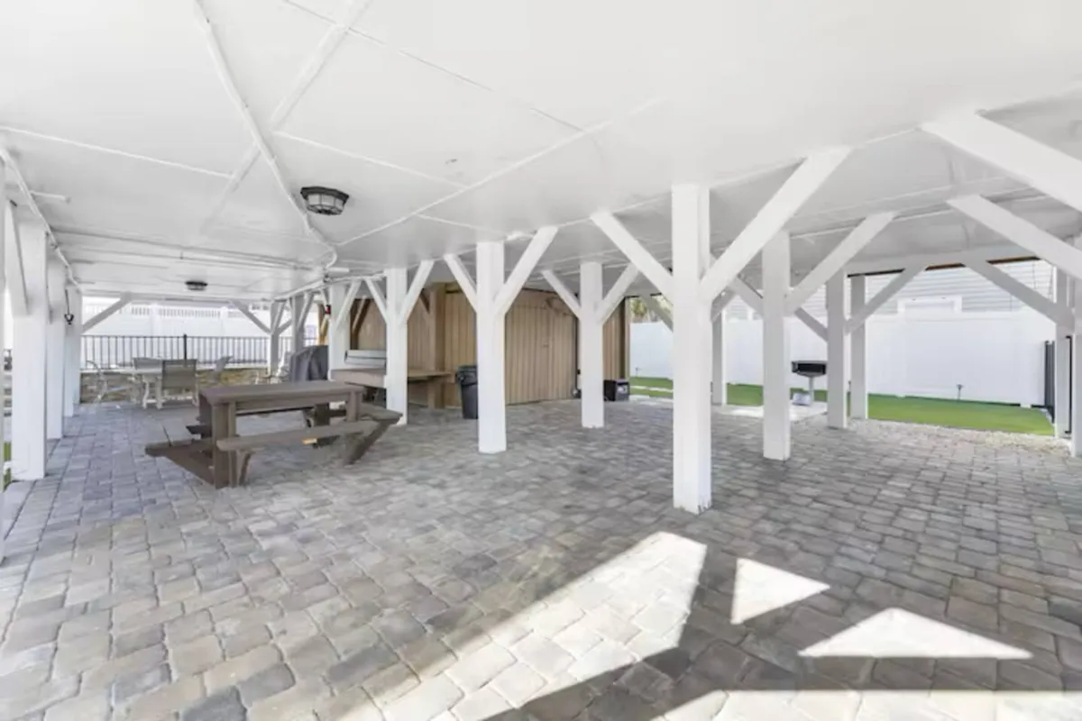 An inviting outdoor area featuring a wooden picnic table under the home, with supporting beams and paved flooring. The space is set up for picnics, spontaneous gatherings, and casual relaxation, hinting at group activities and easy transitions between home and local exploration.