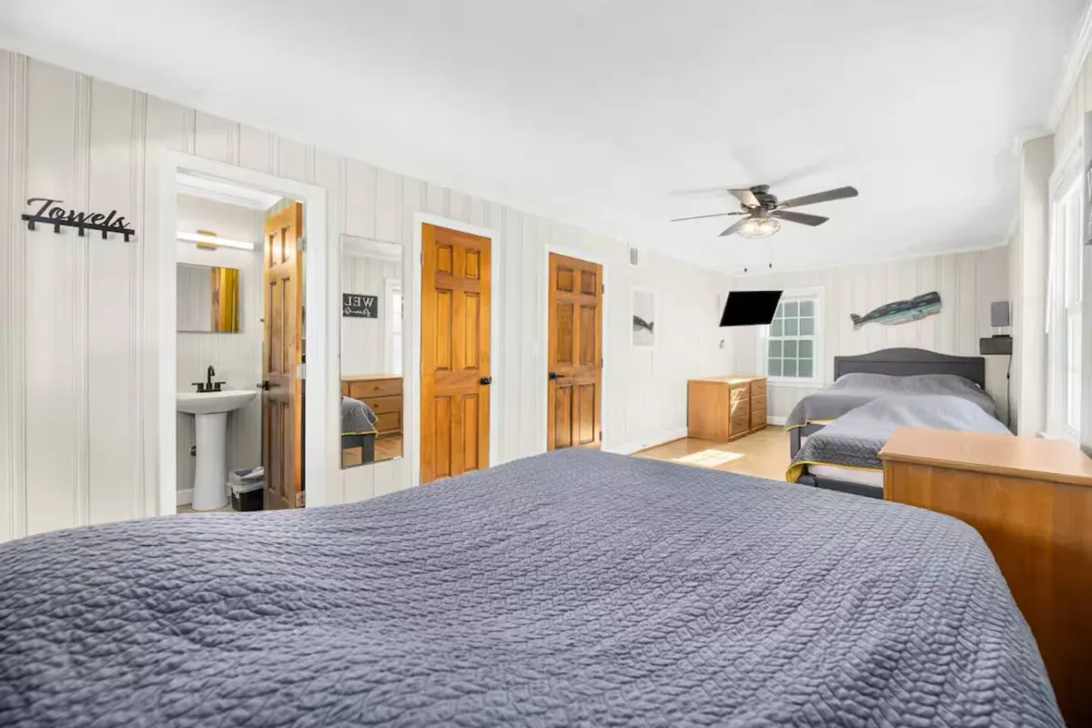 The image features two large beds, wooden furniture, a wall-mounted TV, and whimsical fish-themed decor, all bathed in natural light. The setup is ideal for families or friends sharing a space, emphasizing comfort and shared experiences.